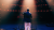 Bradley Jago performing on stage under red and white spotlights, viewed from behind.