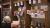 A participant photographs a display of metal foil embossing artworks suspended from strings attached to wooden shelving inside a pub venue. The embossed pieces feature intricate designs in a variety of colours and patterns, with bottles and glassware visible on the shelves below.