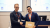 Westminster Master's student Daniel Hernandez Gramajo shakes hands with Mobito CEO, George Cambanis, while one holds a large envelope, with presentation screens and a lectern in the background.