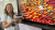 Professor Dr Emily Falconer holding a cake beside a screen displaying fruit and vegetables and the date of the Food and Taste Studies at Westminster launch.