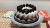 Chocolate bundt cake dusted with icing sugar and topped with fresh blackberries on a patterned plate.