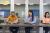 Three students sitting, reading off papers into microphones.