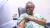 Photo of a woman in a green hospital gown rolling up her sleeve to receive a blood test.