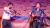 A musician playing a violin and a musician playing a guitar and singing into a microphone in front of a Transgender Pride flag