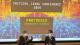 Ingrid Guardiola Sánchez and Julia Chryssostalis seated on stage take part in a discussion in front of a large projected conference slide. The screen displays the text “Critical Legal Conference 2026” and “Protocols: Infrastructures of the Normative,” with a colourful digital graphic background. Both speakers hold microphones while seated facing each other, and the presentation fills the backdrop of the conference venue.