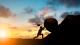 Silhouette of man pushing a rock on a hill