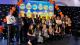 Participants holding awards and smiling in front of a balloon arch