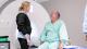 Picture of a man in green hospital robes preparing for an MRI scan with a nurse.