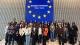 Group photo of student attendees at the European Commission visitor centre. They are standing in front of a blue EU flag.