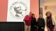 Photo of the organising team of The Benn Legacy event standing in front of a projector displaying the conference's logo, a black and white picture of Tony Benn smoking a pipe surround by the text THE BENN LEGACY UNIVERSITY OF WESTMINSTER 2025