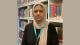 Picture of Dr Monal Mohammed in a library with bookshelves behind her and beige borders on either side of the image.