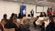 Elias Centellas and Felix Fabiny stand at the front of the room in front of an EU flag and a banner displaying the EU logo. Students sit in rows in front of them to begin the Q and A session.