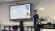 Gareth Bowen speaking in front of a large TV screen displaying nutritional information.