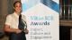 Kate Theophilus holding the Vitae ICE Award trophy in front of a white banner with blue text reading: Vitae ICE Awards Impact, Culture and Engagement