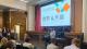 Kayla introducing the first panel discussion in front of a projector screen with the panel topic and panellists' pictures