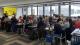 A full room of people at tables listening to a talk on "Keep It Super Simple"