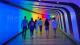 People walking in a subway lit with rainbow colours