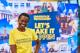 A student ambassador in a yellow t-shirt smiling in front of 'let's make it happen' poster