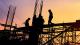 Shadow of construction workers on site against a sunset background.