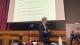 Sir Richard Arnold delivering his lecture in front of a projector screen.