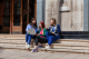 three women sitting on steps, looking at a laptop