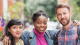 Three smiling students stand together outdoors with their arms around each other.