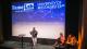 Success Ajayi presenting at the FameLab London Final on a stage with the judges sat on the right