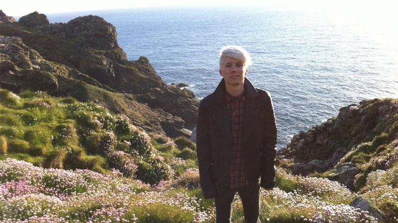 Alumni Gabriel Green standing with the view of rocks and the sea in Cornwall