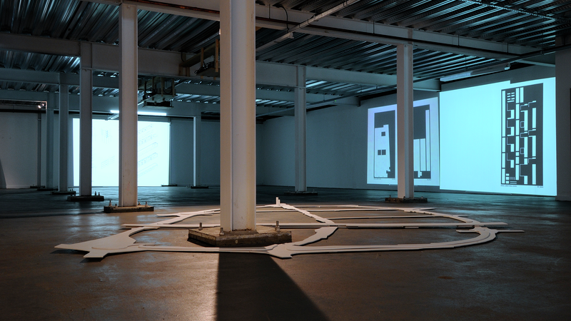 A large gallery space, with a projection on the walls and an exhibit on the floor