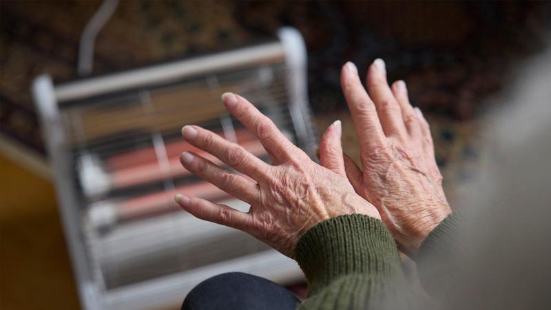 Old hands being warmed at an electric heater