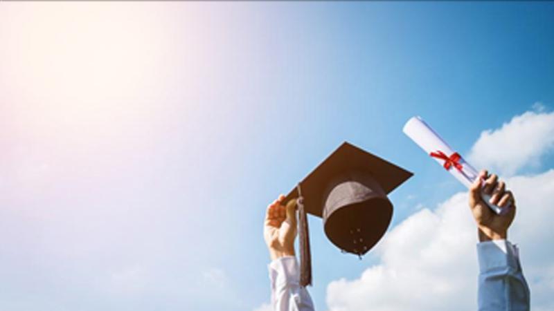 A graduate lifts their cap and scroll in the air