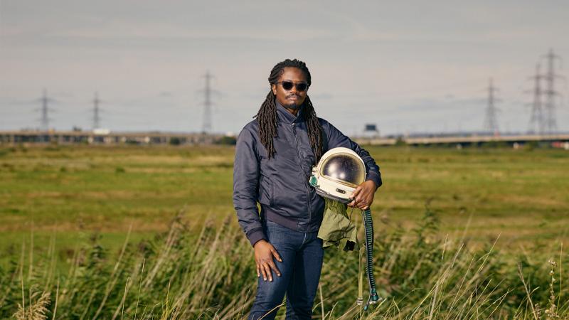 Larry Achiampong holding a motorbike helmet in a field
