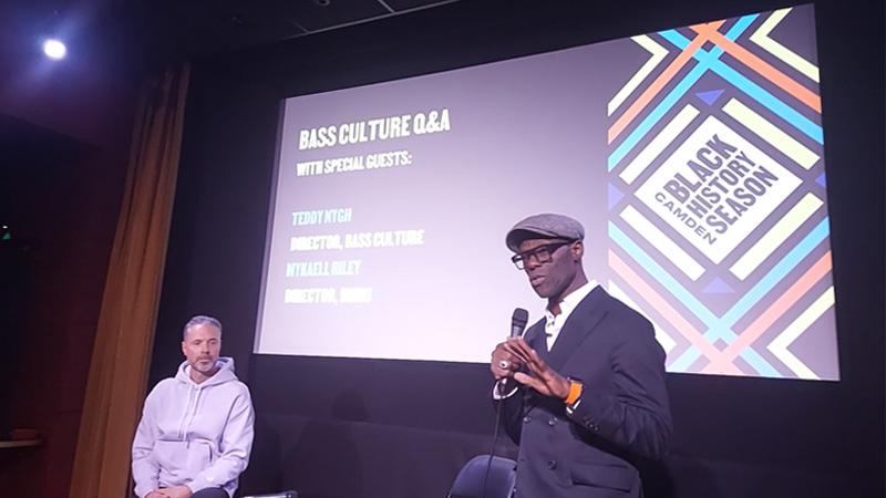 Dr Mykaell Riley speaks to the audience in front of a cinema screen with the title: Bass Culture Q&A. Teddy Nygh sits on the left of the screen.