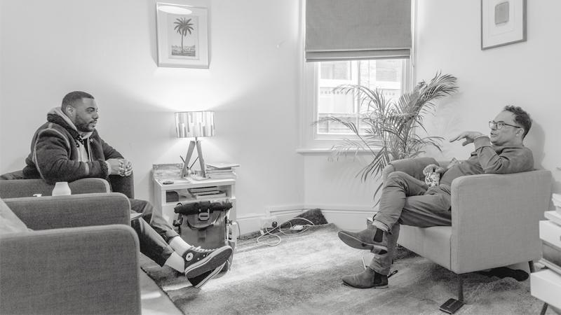 Black and white image of two people talking in therapists office by Ryan Prince