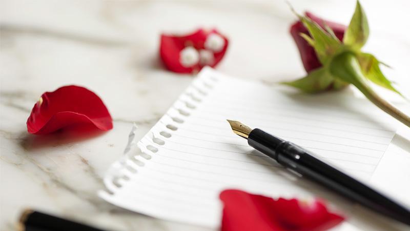 Rose petals on a lined piece of white paper and an ink pen