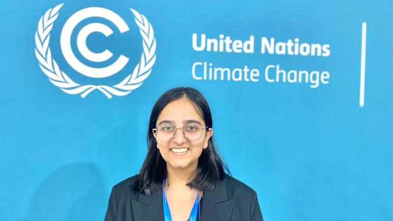 Shriya Gupta stands in front of a blue wall with white text that says United Nations Climate Change