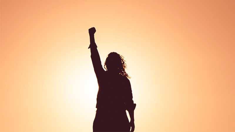 Person celebrating with fist in the sky and sunset background