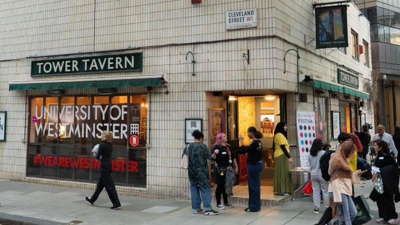 Exterior view of the Tower Tavern on Cleveland Street in London, with several people gathered outside the entrance. University of Westminster branding is displayed in the front windows, and event attendees are arriving and socialising on the pavement.