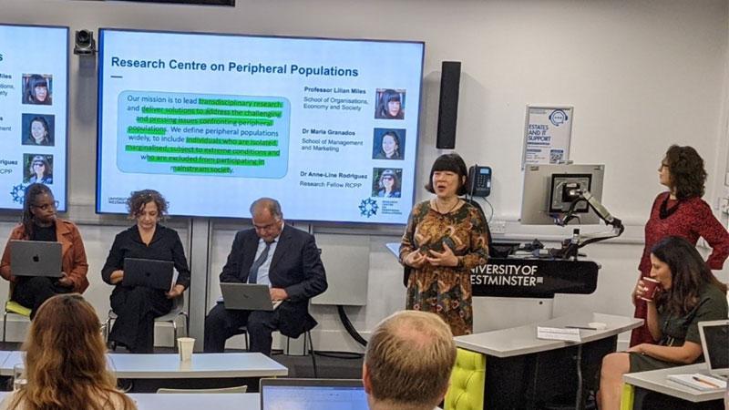 Panellists of the event sit in front of a whiteboard displaying the research centre's mission statement. On the right of the screen, Professor Lilian Miles addresses the audience. To her right, there are Dr Maria Granados and Dr Anne Line Rodriquez.