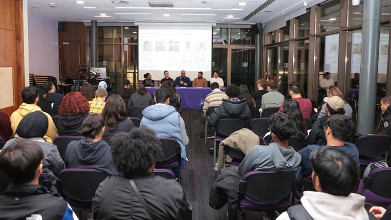 A photo from the back of the audience showing rows of people in front of a panel of alumni.