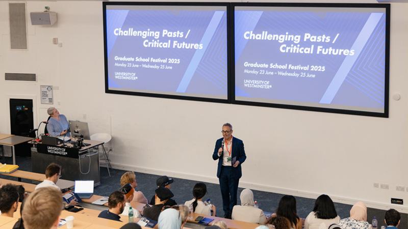 Andrew Linn opening the Graduate School Festival in front of two large screens reading Challenging Pasts, Critical Futures
