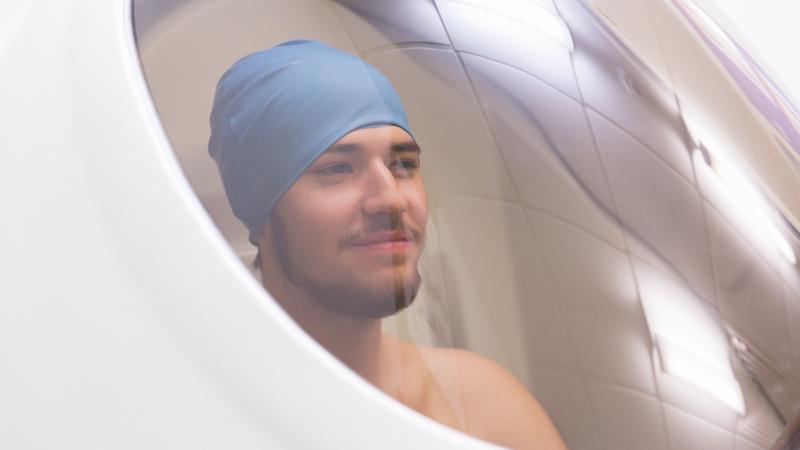 An athlete sitting in the BodPod chamber - a pod with a glass window. The athlete is smiling.