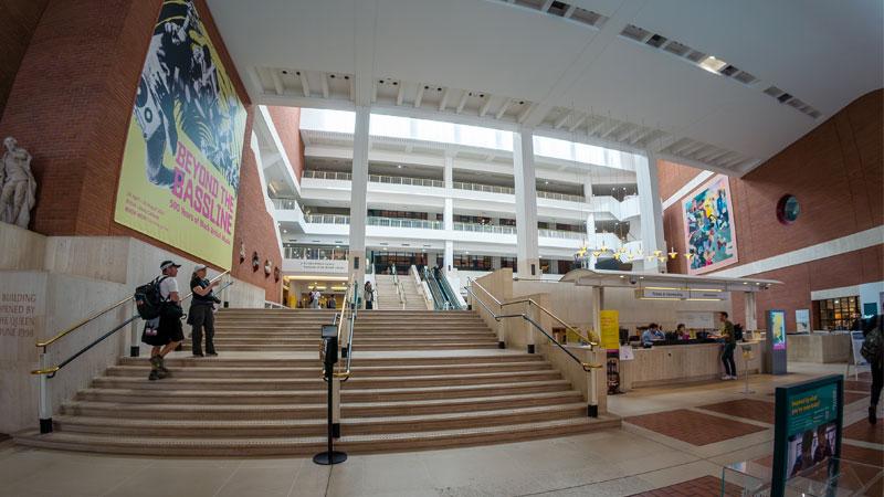 Wide lens photo of the British Library reception with a large poster of the Beyond the Bassline exhibit on the left hand side.