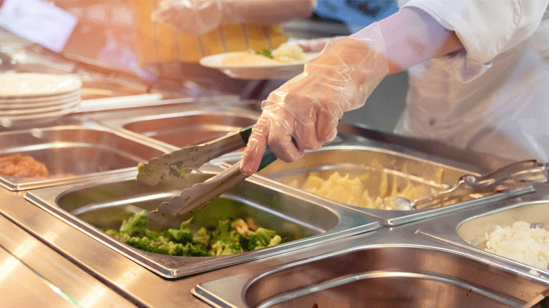 Chef standing behind full lunch service station with assortment of food in trays