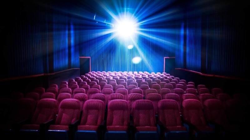 Stock photo of a cinema screening room with the bright light from the projector shining brightly from the back of the room