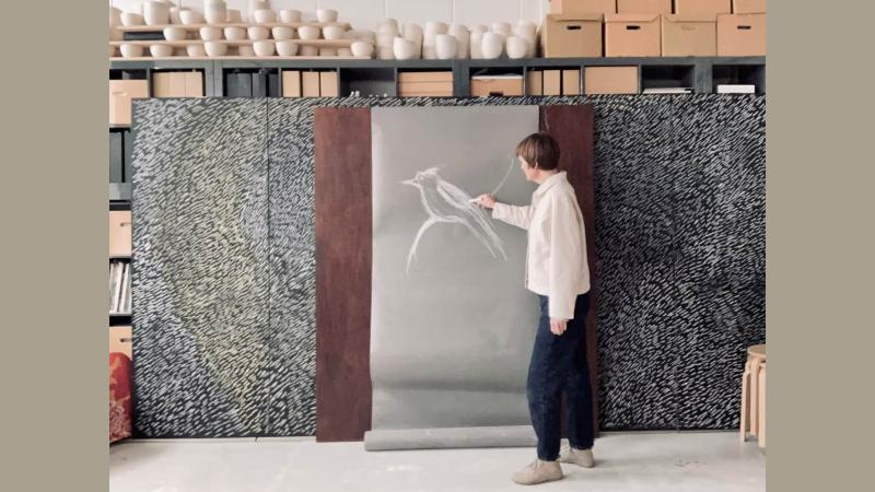 Picture of Clare Twomey in her studio making a sketch of a bird with chalk.