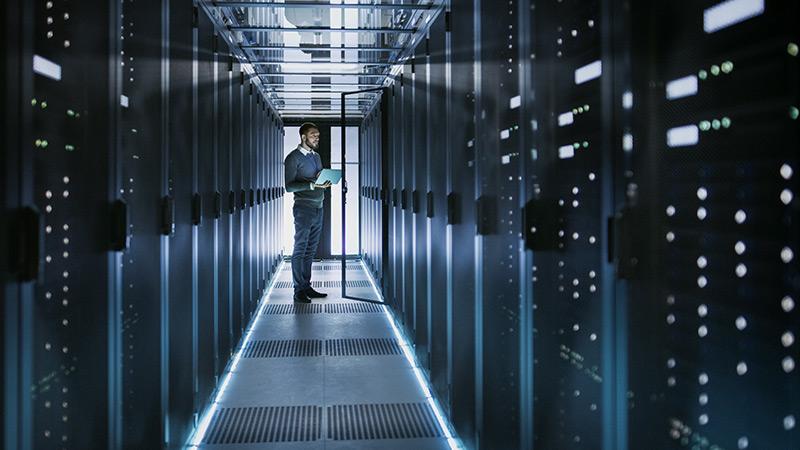 IT Technician Works on Laptop in Big Data Center full of Rack Servers