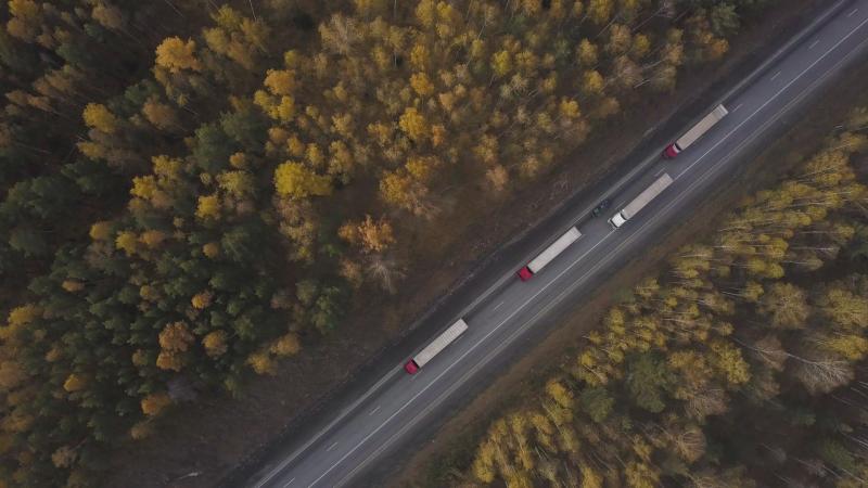 Stock image of drone shot of freight trucks driving down a road surrounded by trees