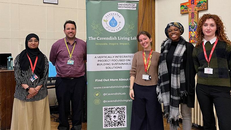 Photo of the Greener Futures Leaders with a teacher from Grey Coat Hospital School. They are standing around a green banner with information about the Cavendish Living Lab