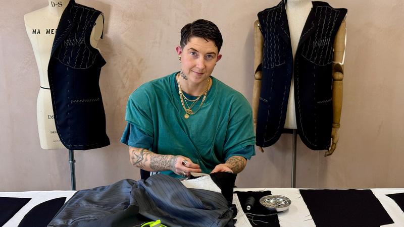 Gia Jenkins sewing at a table in front of two mannequins.